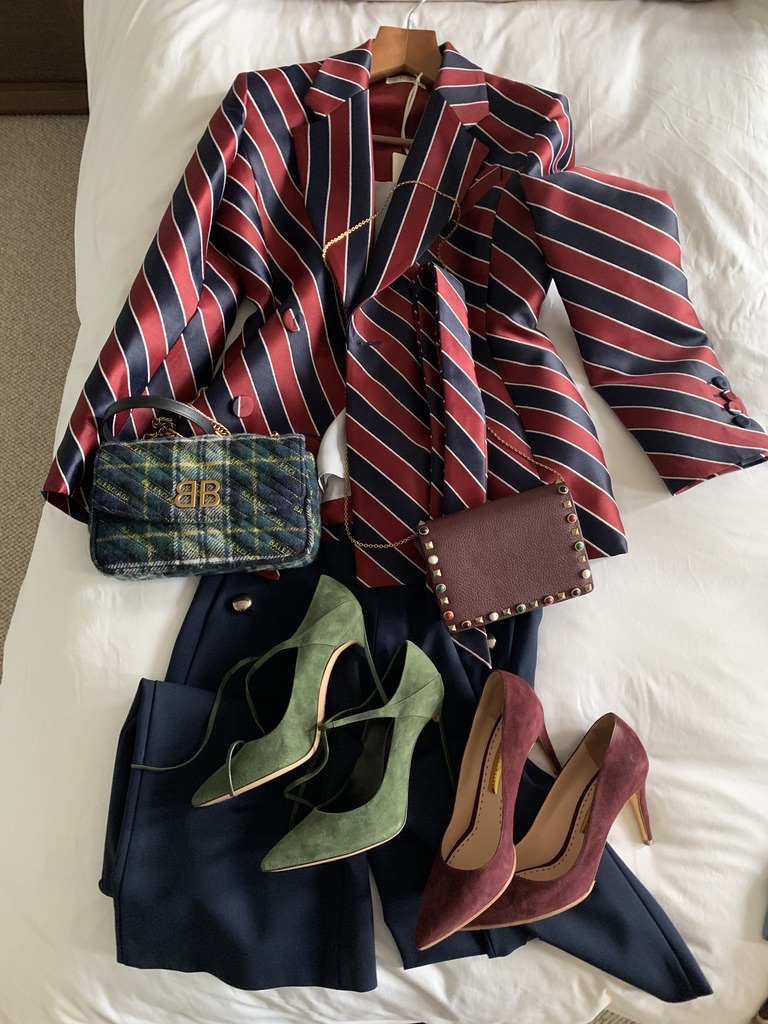 A striped jacket, trousers, shoes and bags arranged together on a bed